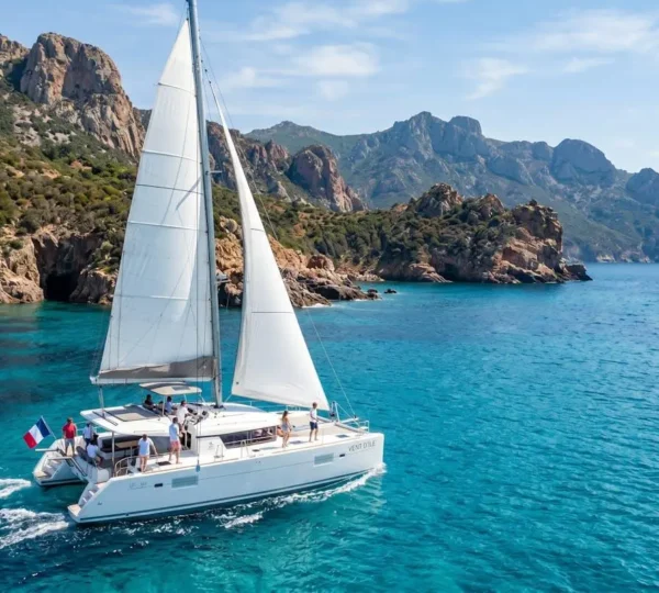Catamaran moderne naviguant dans les eaux cristallines de Corse avec la côte rocheuse en arrière-plan