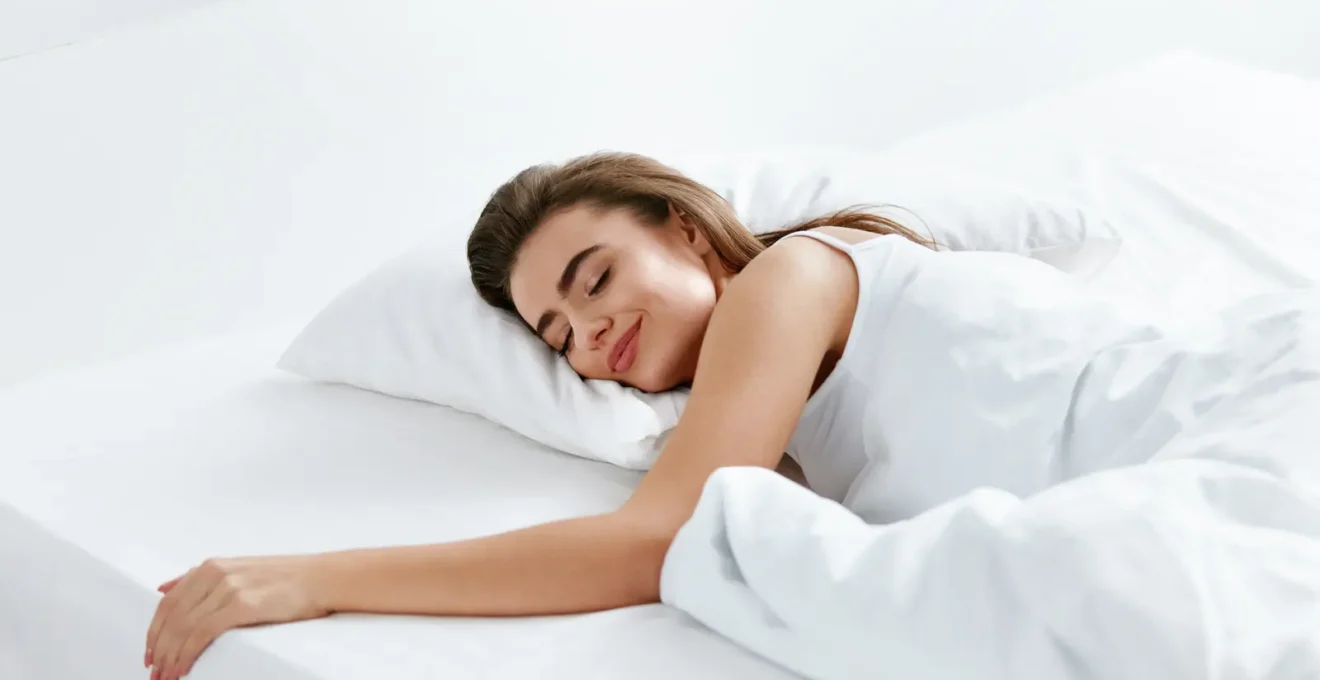 Une conseillère de vente teste un matelas sur le dos dans un magasin de literie pendant qu'un vendeur vérifie le soutien lombaire avec sa main.